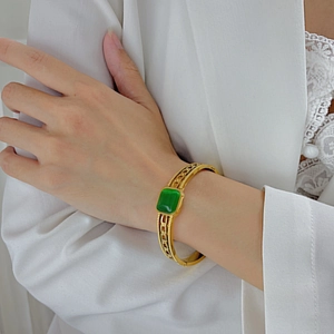 Vintage gold hollow chain bracelet with rectangular green gemstone worn on white suit