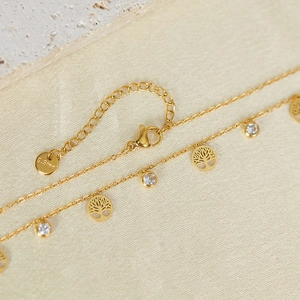 Close-up of golden tree of life anklet with white zircon stones on stone base