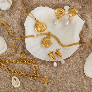 Set gioielli dorati a tema oceano con conchiglie e stelle marine su sabbia