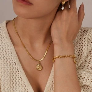Dettaglio della collana con conchiglia dorata e orecchini di perle su maglia