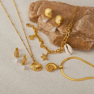 Set gioielli tema oceano in acciaio dorato con conchiglie, stelle marine e perle sulla sabbia