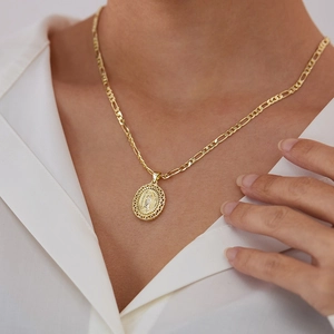 Detailweergave van de ovale Maria-hanger aan een gouden Figaro-ketting op een model