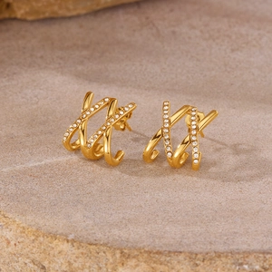 Detail shot of golden triple-layered crossover stud earrings with zircons on stone background