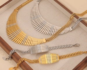 Détail de parure bijoux gourmette or et argent avec pendentifs à grille strassée
