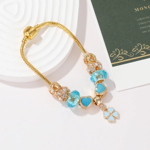 Dettaglio del bracciale dorato con ciondolo a quadrifoglio blu e perline a forma di cuore