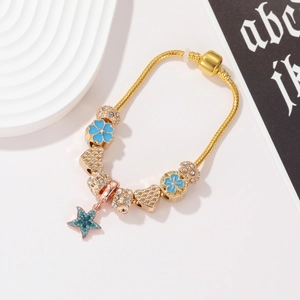 Dettaglio del bracciale a maglia serpente dorata con fiori in smalto blu e ciondoli stella