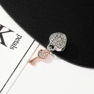 Macro shot of silver heart lock charm and rose gold key pendant with pavé crystals