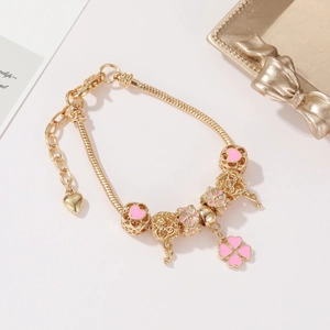 Detail of golden snake chain bracelet featuring pink enamel heart charms and clover pendant