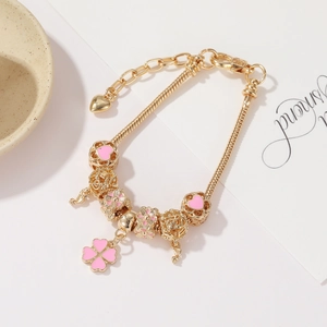 Detail of gold snake chain bracelet with pink enamel clover and heart charms
