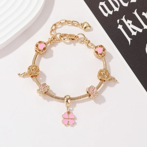 Detail of golden charm bracelet with pink clover pendant and hollow heart beads