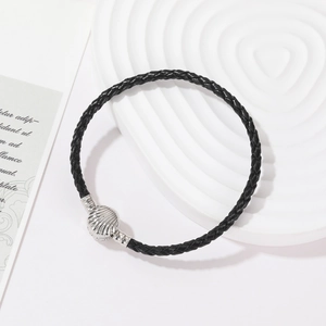 Handgeweven zwarte lederen armband met een zilveren schelp sluiting op een wit bord