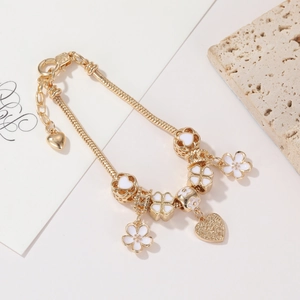 Detailed macro view of gold-tone snake chain bracelet with white floral charms and heart pendants