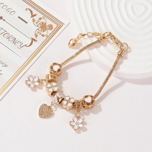 Macro shot of gold snake chain bracelet with white enamel flower and heart charms