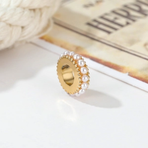 Dettaglio macro di un ciondolo dorato con perle bianche e trama a ingranaggi su bianco