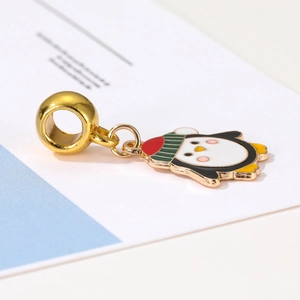 Macro detail of enamel penguin charm with striped hat on golden slider bead