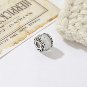 Close-up of translucent glass charm with ornate silver floral filigree and vintage background