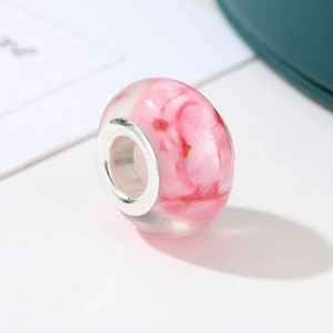 Macro shot of pink resin charm bead with floral patterns and silver metal core detail