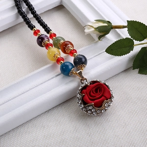 Dettaglio di un ciondolo a rosa rossa in tessuto con cristalli su collana di perline colorate