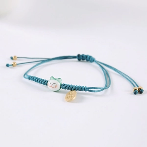 Dettaglio bracciale blu intrecciato con gatto portafortuna in ceramica e ciondolo