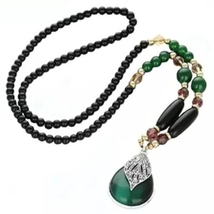 Long collier bohème en perles avec pendentif goutte verte sur fond blanc épuré