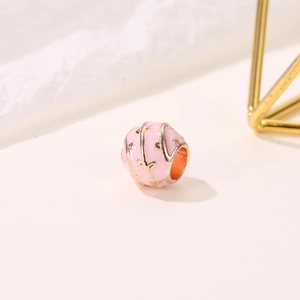 Macro-opname van roze emaille bedel met roségouden wijnstokpatronen voor DIY-armbanden