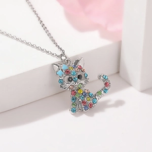 Dettaglio della collana con ciondolo a forma di gatto e strass colorati su base bianca chic
