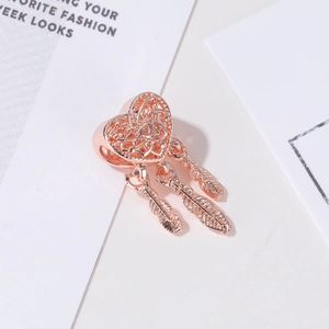 Rose gold heart dreamcatcher charm with three feather pendants on fashion magazine