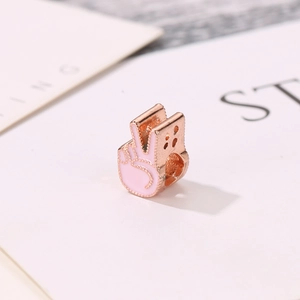 Macro d'une breloque geste de victoire en or rose et émail rose pour bracelets DIY