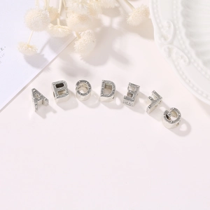 Detalle de cuentas plateadas DIY con letras y textura de puntos para hacer joyas