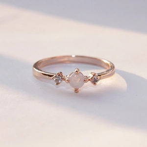 Rose gold engagement ring featuring a central round white opal and side zircon accents