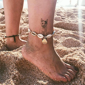 Handmade shell anklet with golden scallop charms and white woven rope on a beach