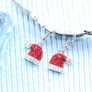 Macro detail of Christmas hat earrings with red and white rhinestones on blue knit sweater