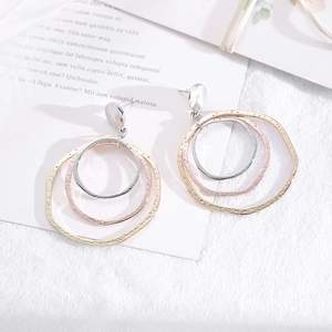 Irregular tricolor metal hoop earrings with hammered texture on white faux fur background