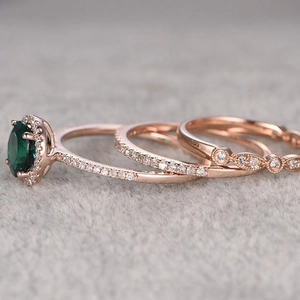 Three-piece rose gold ring set featuring a large round emerald and halo diamond accents