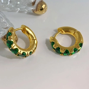 Elegante goldene Huggie-Ohrringe mit smaragdgrünen Kristallen auf weißem Grund