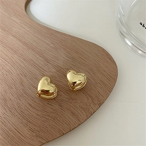 Detailed view of 3D heart hoop earrings in gold finish on a natural wooden tray