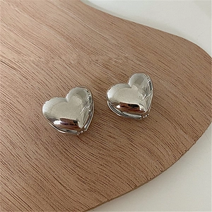 Detailed view of polished silver heart-shaped hoop earrings on a minimalist wooden tray