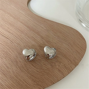 Detail of silver heart-shaped earrings on a natural wood tray with white background