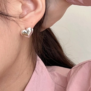 Macro shot of a minimalist 3D heart-shaped silver stud earring on a model's ear