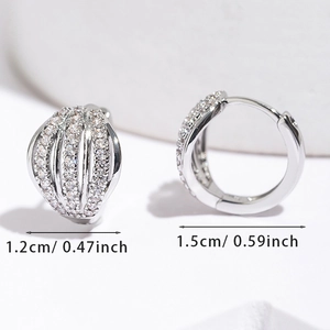 Détail de boucles d'oreilles créoles argentées en forme de coquillage pavées de zircons