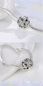 Close-up of silver clover charm with vintage heart pattern on a snake chain bracelet
