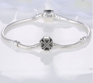 Detailed macro view of silver clover heart charm on a polished snake chain bracelet