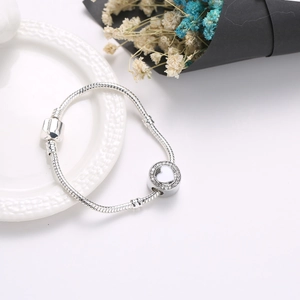 Zilveren snake chain armband met hartvormige hanger op een decoratief keramisch bord