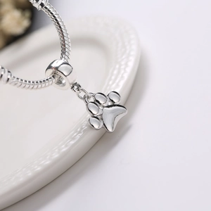 Poliertes Silber Schlangenarmband mit Pfotenanhänger auf einem eleganten Keramikteller