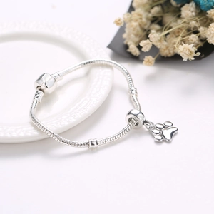 Silbernes Schlangenarmband mit Pfotenabdruck-Anhänger auf einem weißen Teller
