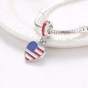 Silver snake chain bracelet with heart-shaped American flag enamel charm on a white dish
