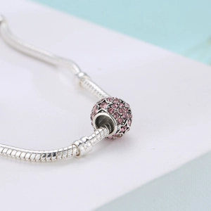 Detailed macro view of a silver snake chain bracelet with a pink crystal star charm