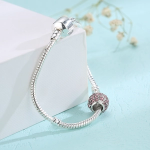 Detail of silver snake chain bracelet featuring pink rhinestone star charm on blue texture
