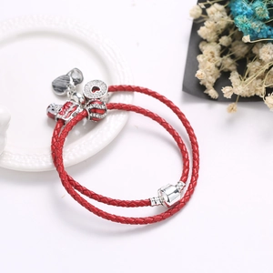 Braided red leather wrap bracelet with silver heart and lion dance charms on a white plate