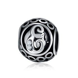 Macro shot of silver hollow charm featuring artistic letter E engraving and clear gemstones